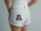white University of Arizona women’s game day denim shorts with lace-up sides, frayed hem, and Arizona Wildcats logo on back pocket