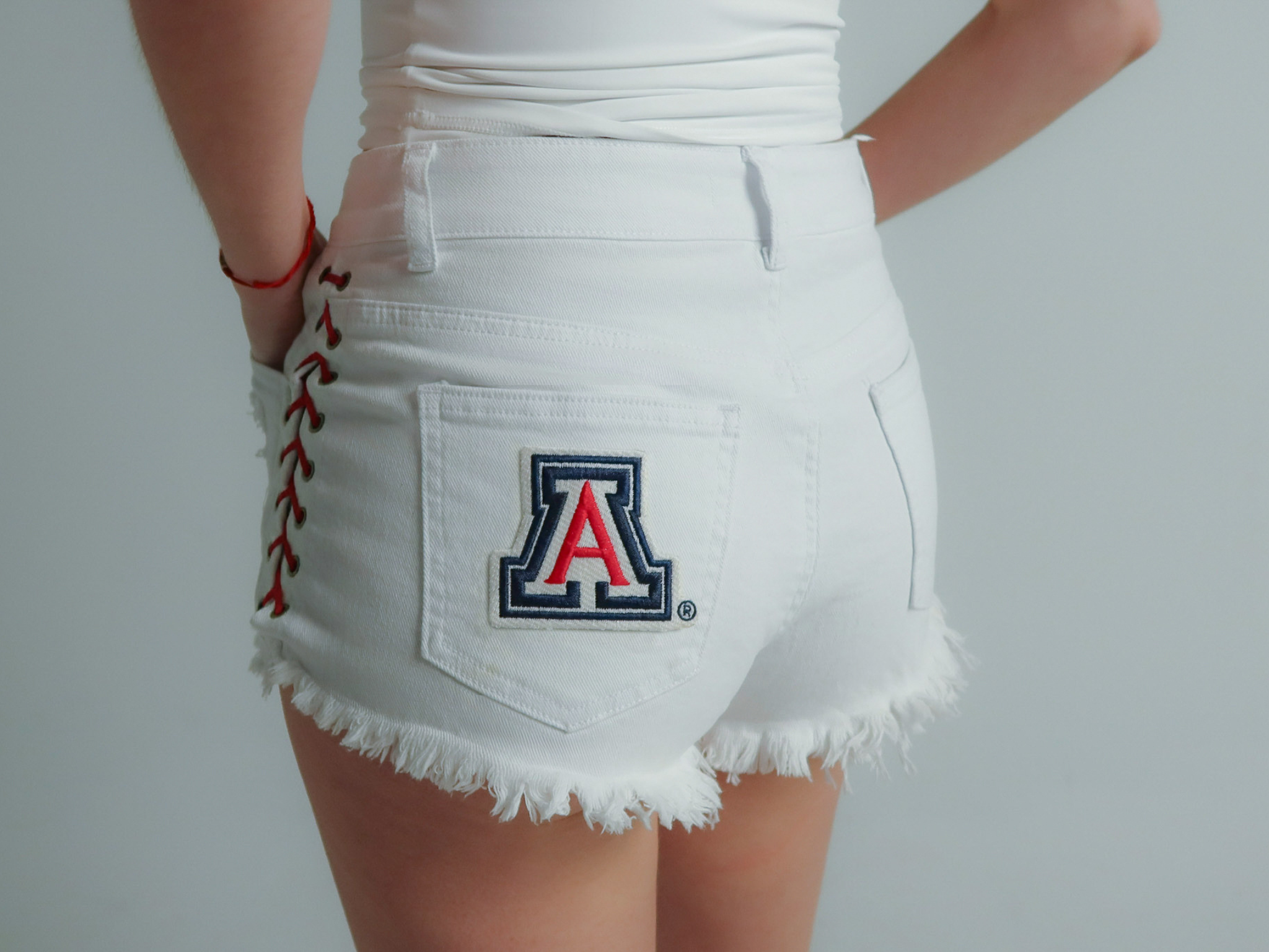 white University of Arizona women’s game day denim shorts with lace-up sides, frayed hem, and Arizona Wildcats logo on back pocket